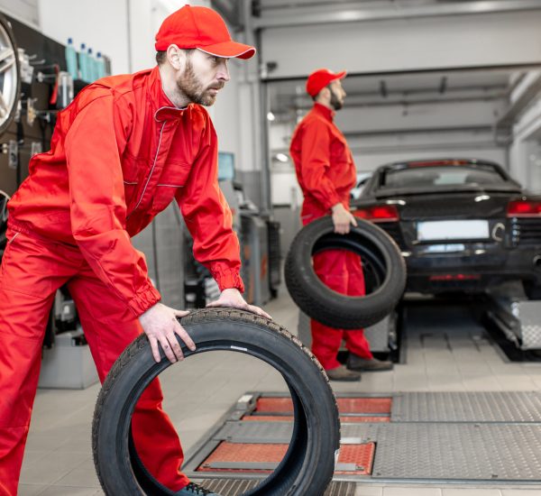 Car service workers in red uniform carrying new tires at the tire mounting service or shop